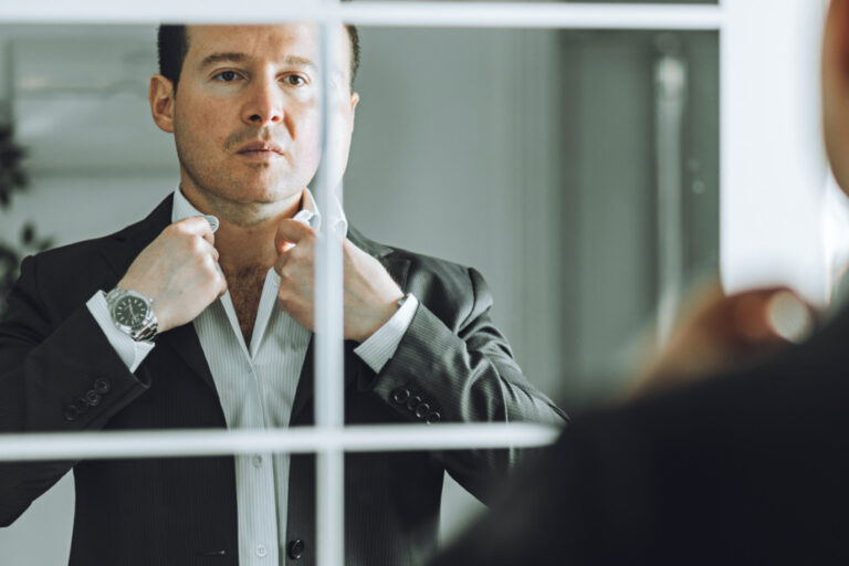 stoic man adjusting his shirt in a mirror reflects the stereotype of how emotionless leadership hinders effectiveness